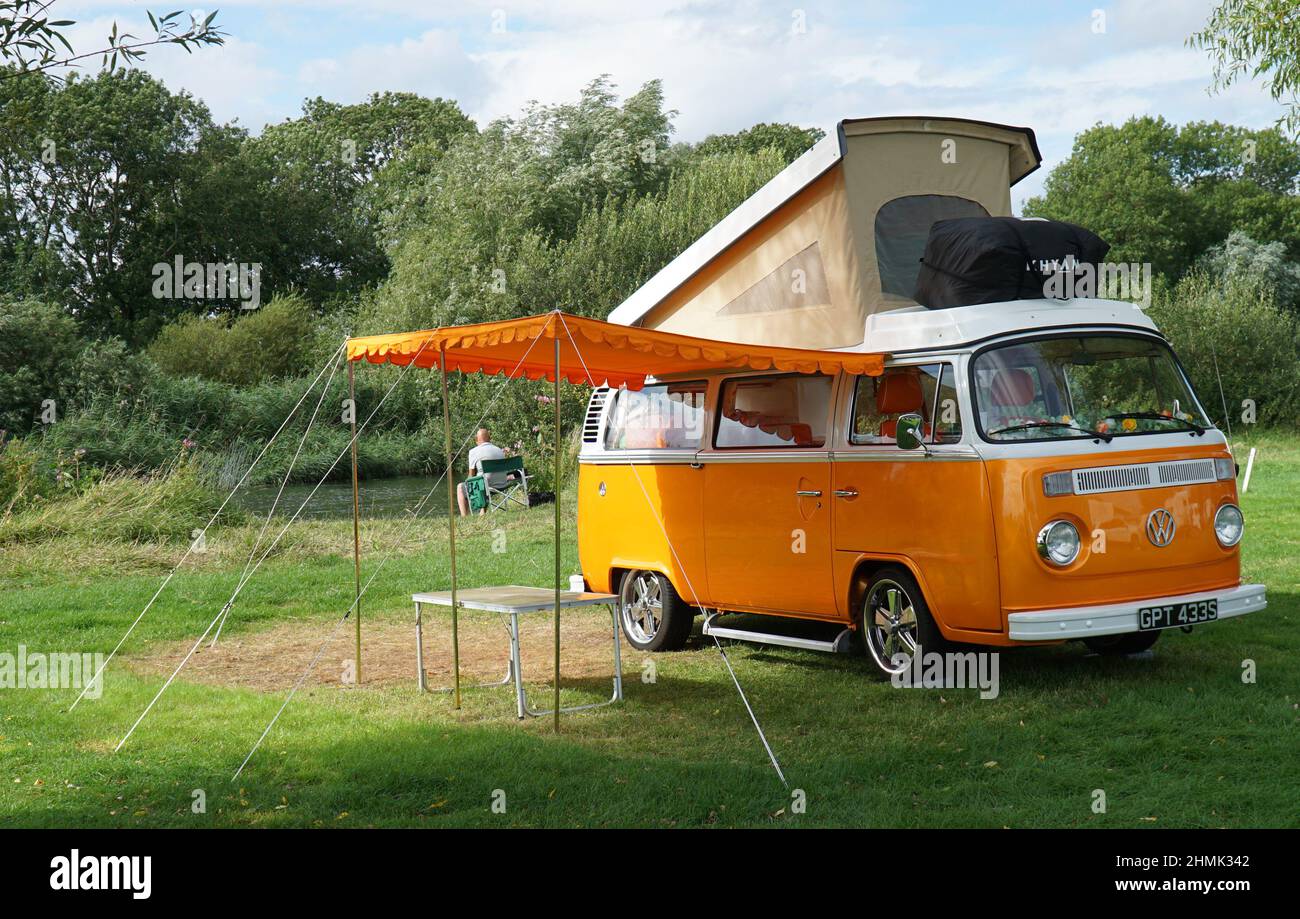 Classic Orange Volkswagen Camper Van, geparkt auf dem Campingplatz am Fluss mit Auflauf und Markisen Stockfoto