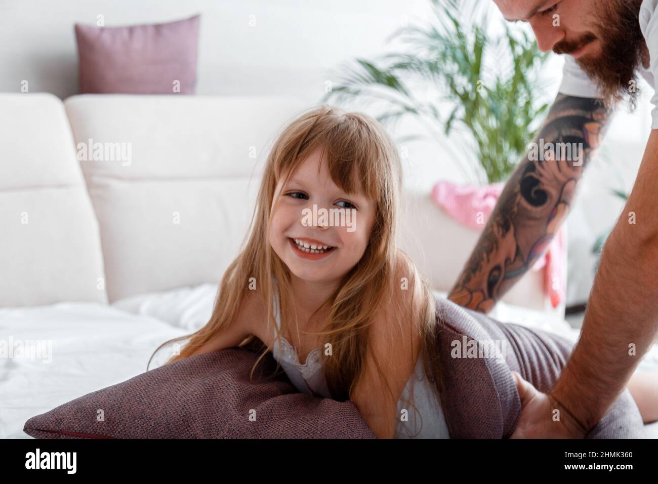 Porträt von Kind Kind Mädchen lacht spielen mit Vater. Vater und Tochter spielen im Schlafanzug im Bett gemeinsam im Kissenkampf. Kahlbärtig Stockfoto