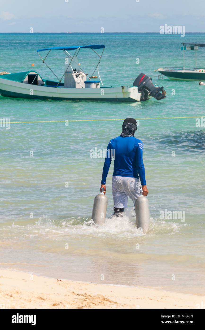 Rückansicht Eines Tauchers trägt Sauerstofftanks mit seinen Händen im Wasser, um sie in das Boot zu laden. Tulum Beach, Mexiko Stockfoto