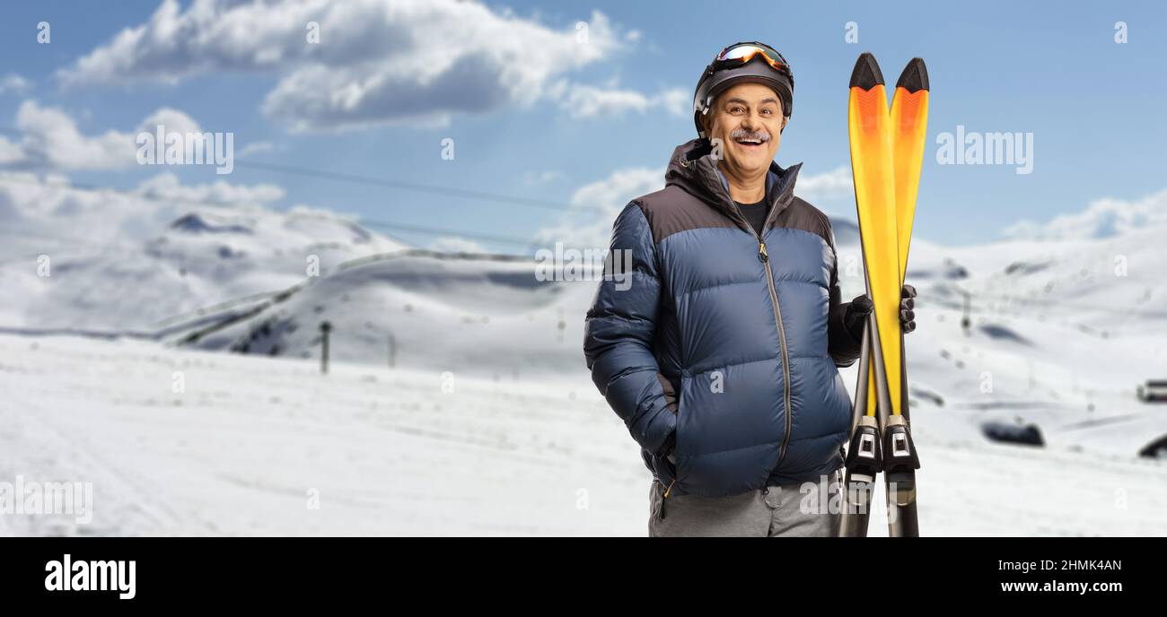 Reifer Mann lächelt und hält ein Paar Ski auf einem Berg Stockfoto