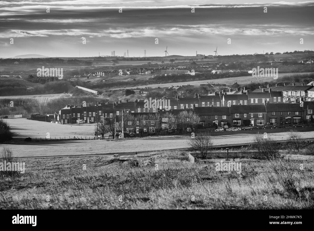 Easington Colliery County Durham Reihen von Reihenhäusern mit einem Biomasse-Zug, der im Hintergrund vorbeifährt und einem mit einer Kappe bedeckten Grubenkopf im Vordergrund Stockfoto