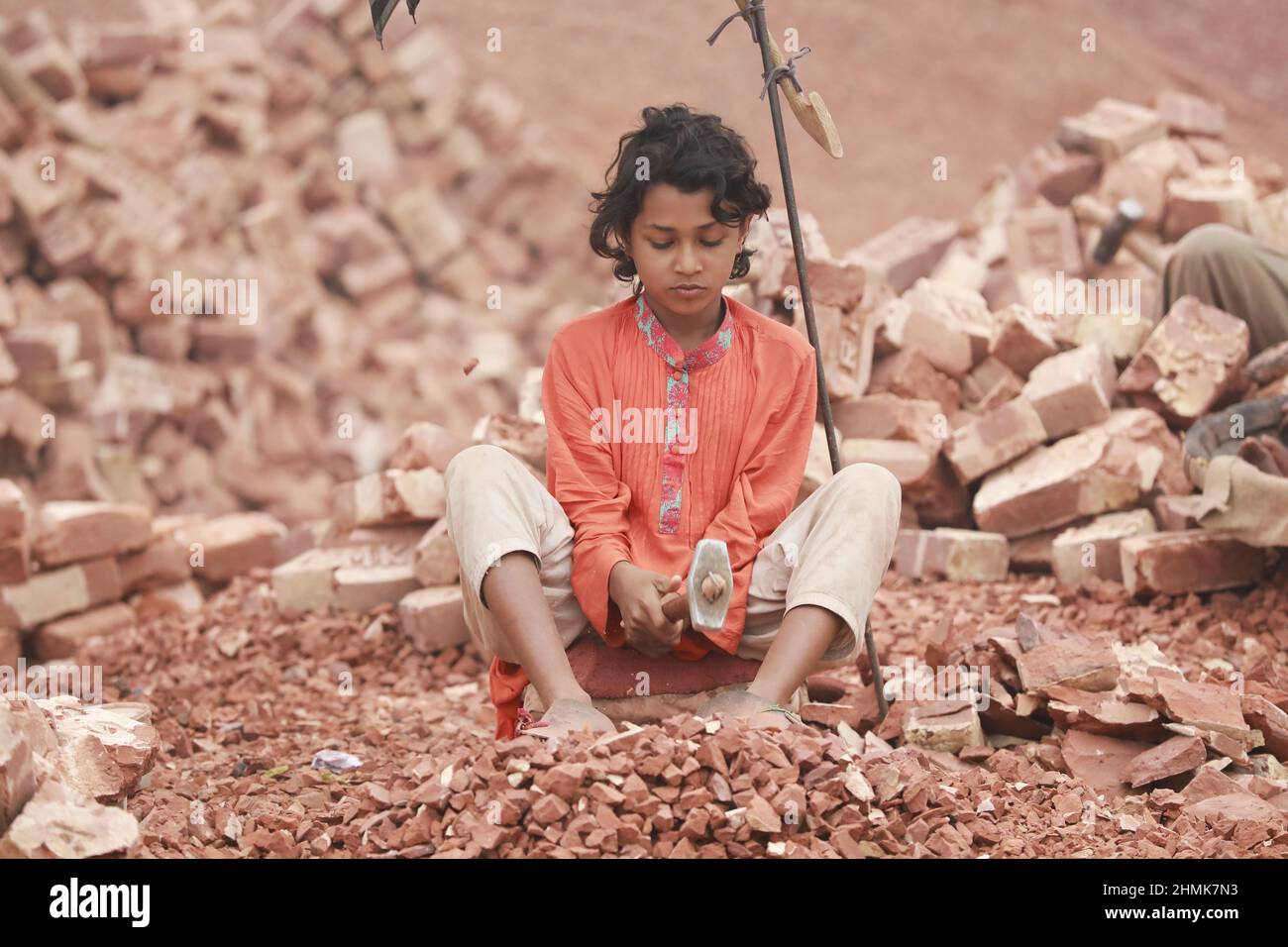 Die Kinder von Bangladesch, Rajiya, 9, brechen Ziegel, die als Kies für den Bau in Dhaka, Bangladesch, verwendet werden sollen, 10. Februar 2022. Kinderarbeit ist in Bangladesch üblich, 4,7 Millionen Kinder im Alter von 5 bis 14 Jahren arbeiten in der Belegschaft. Von den Kinderarbeitern, die in der Belegschaft beschäftigt sind, sind 83 % in ländlichen Gebieten und 17 % in städtischen Gebieten beschäftigt. Im Jahr 2006 verabschiedete Bangladesch ein Arbeitsgesetz, in dem das Mindestalter für eine Beschäftigung auf 14 Jahre festgelegt wurde. Dennoch ist die Durchsetzung solcher Arbeitsgesetze in Bangladesch praktisch unmöglich, da 93 % der Kinderarbeiter im informellen Sektor wie Smal beschäftigt sind Stockfoto