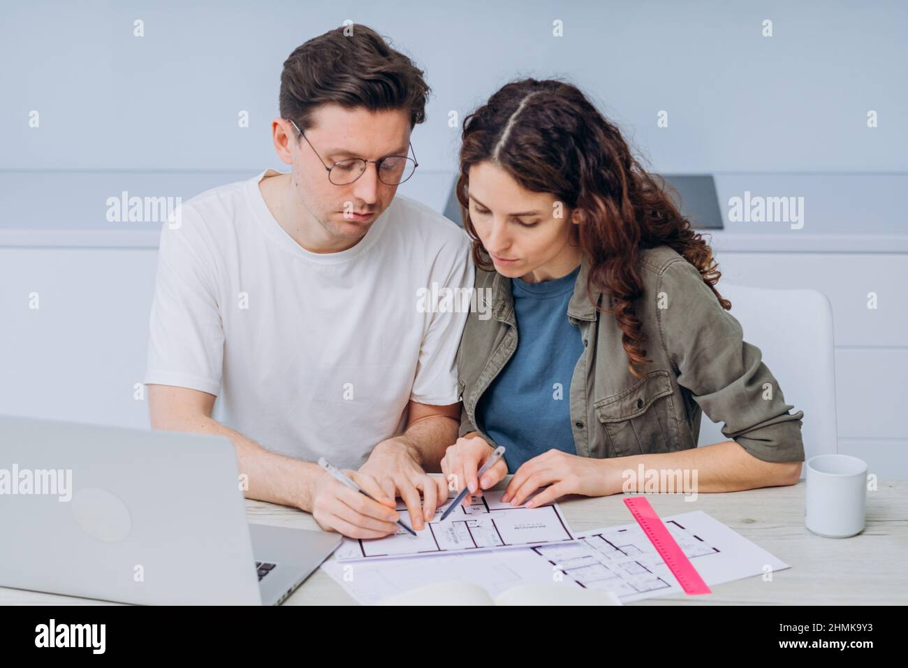 Das Paar sitzt in der Küche, trinkt Kaffee zum Frühstück und spricht über Zeichnungen von Wohnungsrenovierungen, die Notizen in Laptop und Notebook machen Stockfoto