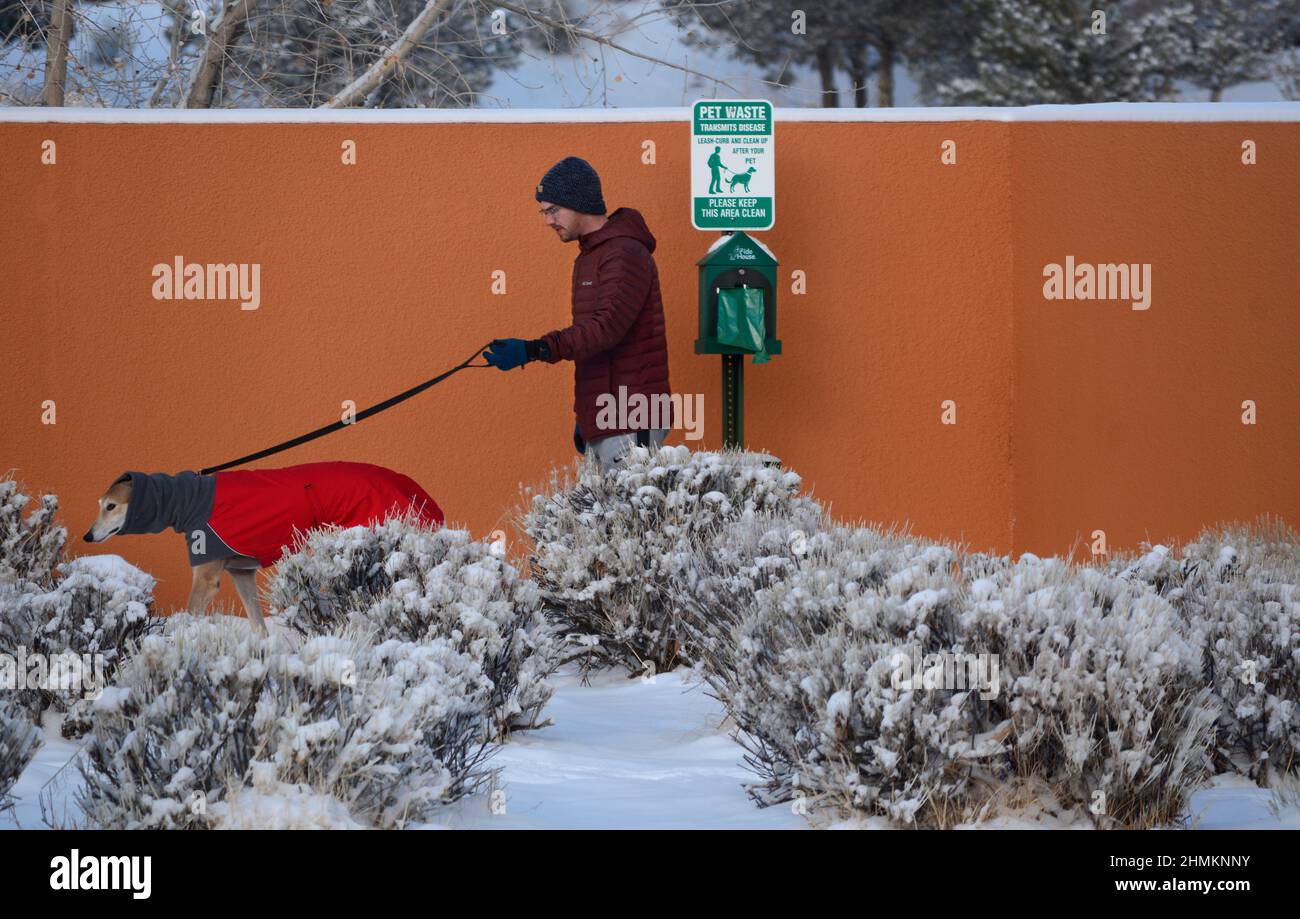 Ein Mann geht in Santa Fe, New Mexico, zu seinem Rettungshund. Der Hund trägt einen Wintermantel und einen Halswärmer oder einen Hundeschnül von Voyager K9 Apparel. Stockfoto