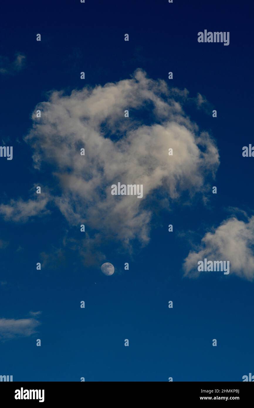 Der Mond teilt sich den blauen Himmel mit verstreuten weißen Wolken über Santa Fe, New Mexico. Stockfoto