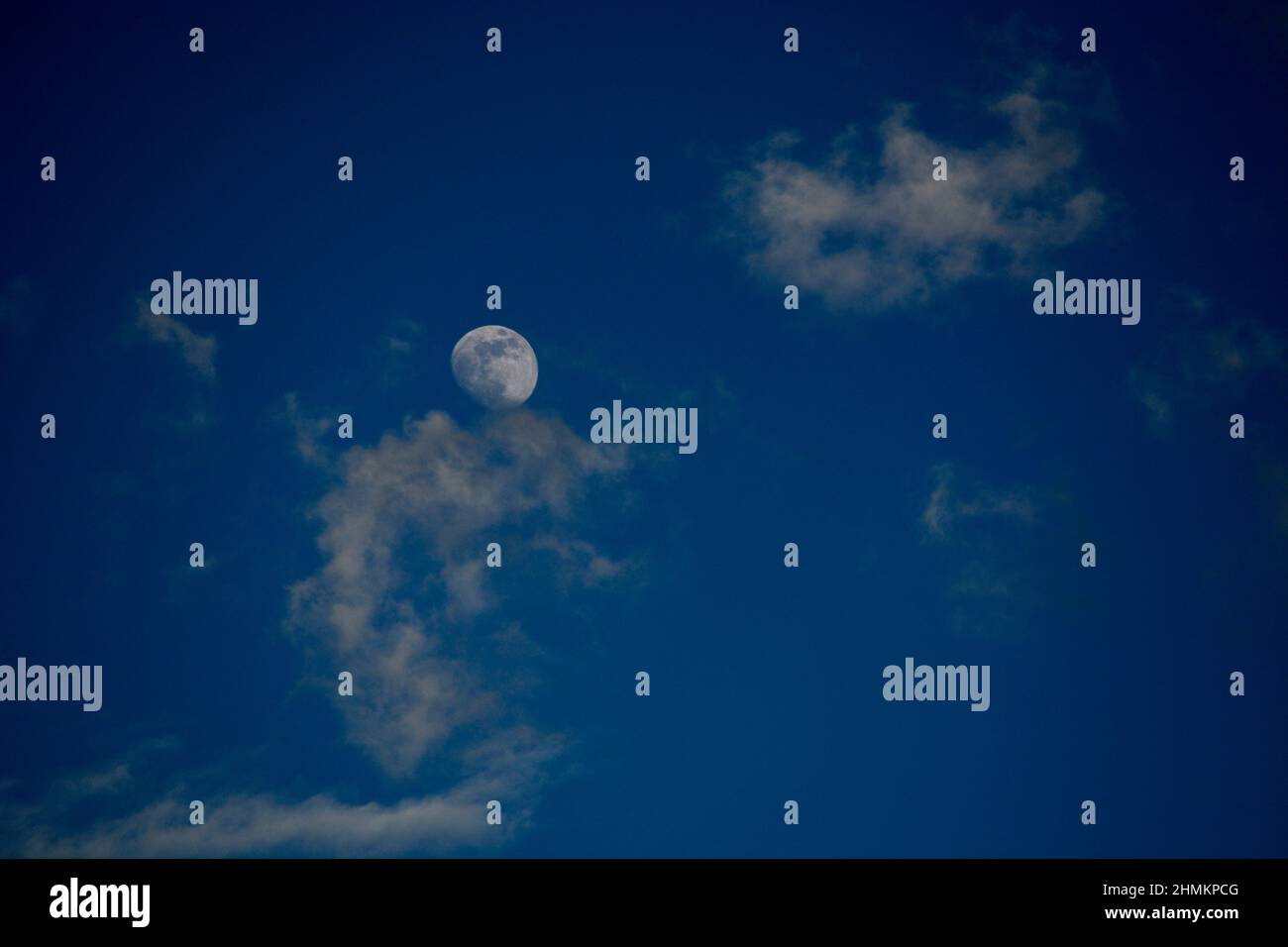 Der Mond teilt sich den blauen Himmel mit verstreuten weißen Wolken über Santa Fe, New Mexico. Stockfoto