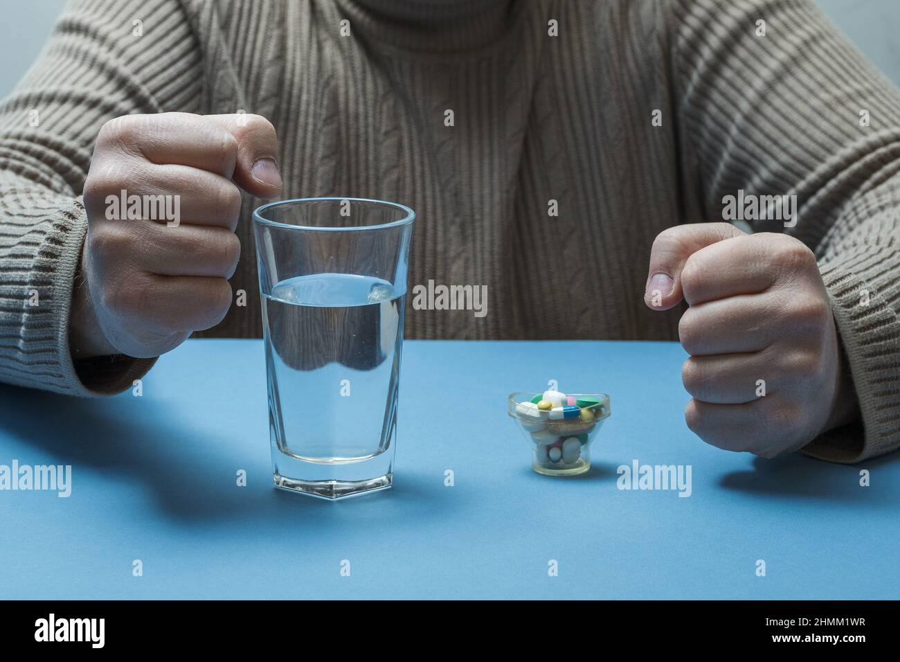 Der Mann schlingt seine Hände zu Fäusten, medizinische Vorbereitungen und ein Glas Wasser stehen vor ihm auf dem Tisch. Stockfoto