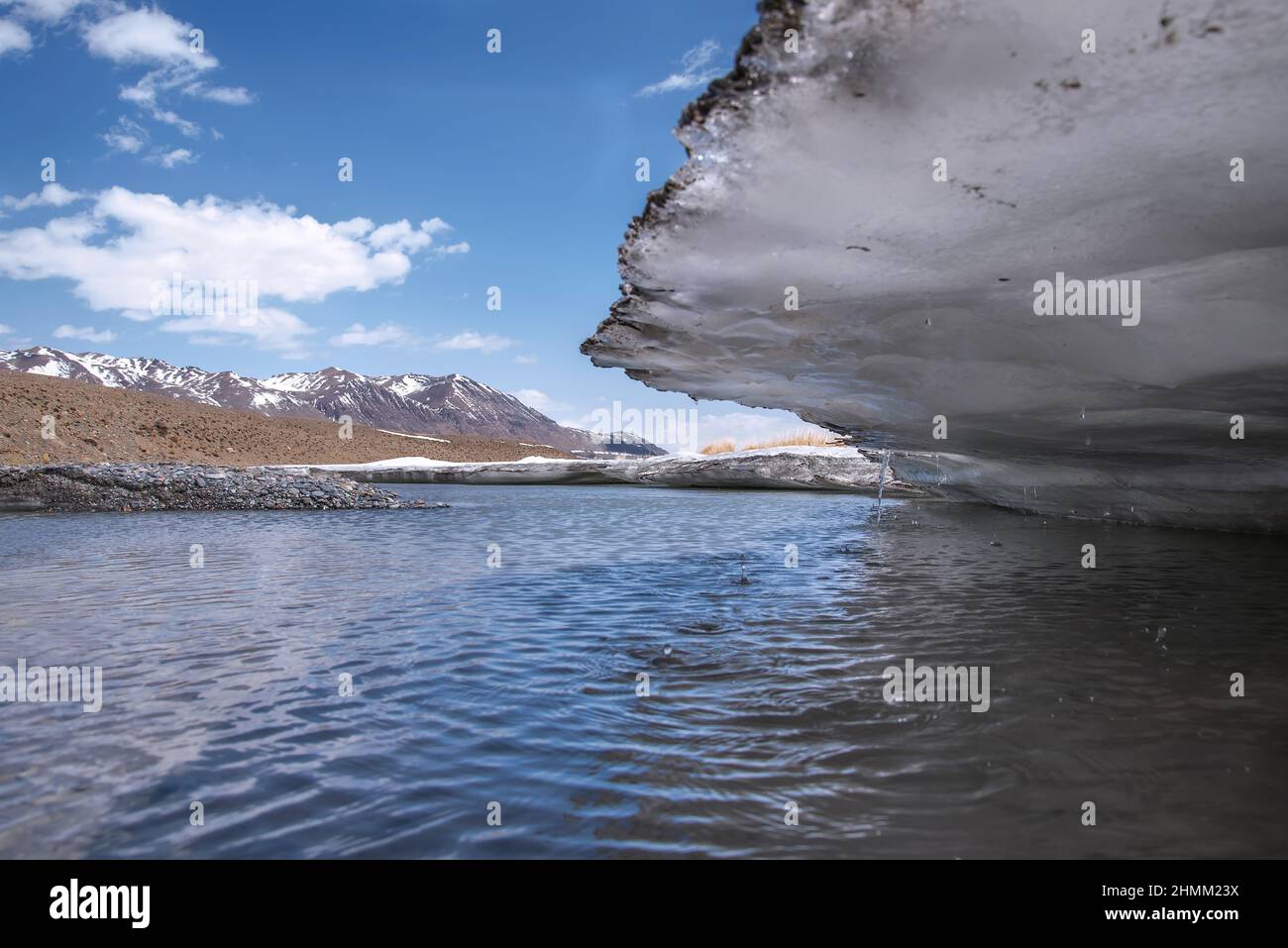Malerischer Frühlingsblick auf einen schnellen Gebirgsfluss und große Eisschollen entlang der Ufer vor dem Hintergrund schneebedeckter Berge, blauem Himmel und Wolken. Alt Stockfoto