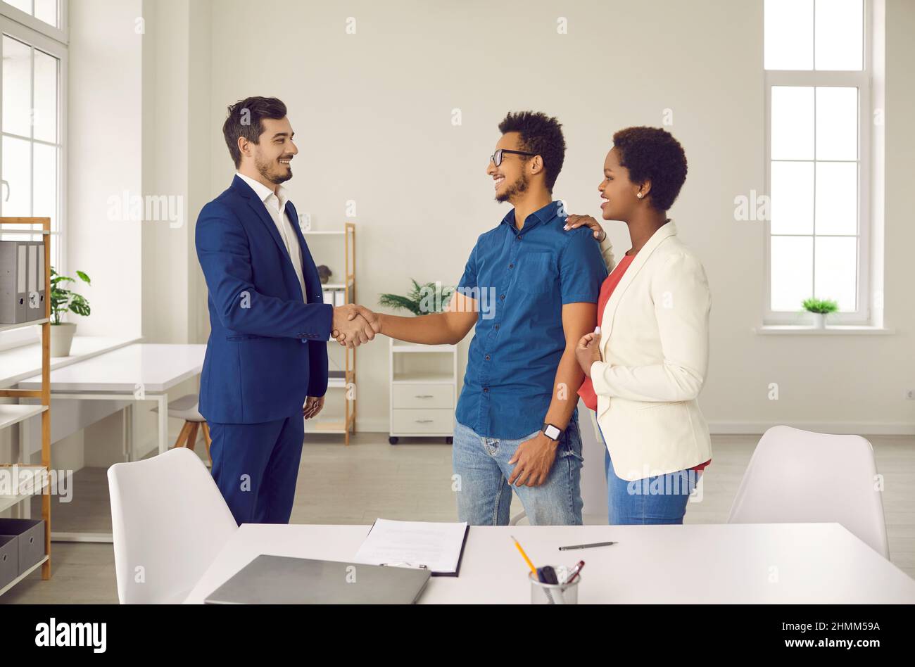 Nach Abschluss eines Bankdeals auf Kredit oder Hypothek schüttelt der Bankagent die Hände mit einem glücklichen Paar. Stockfoto