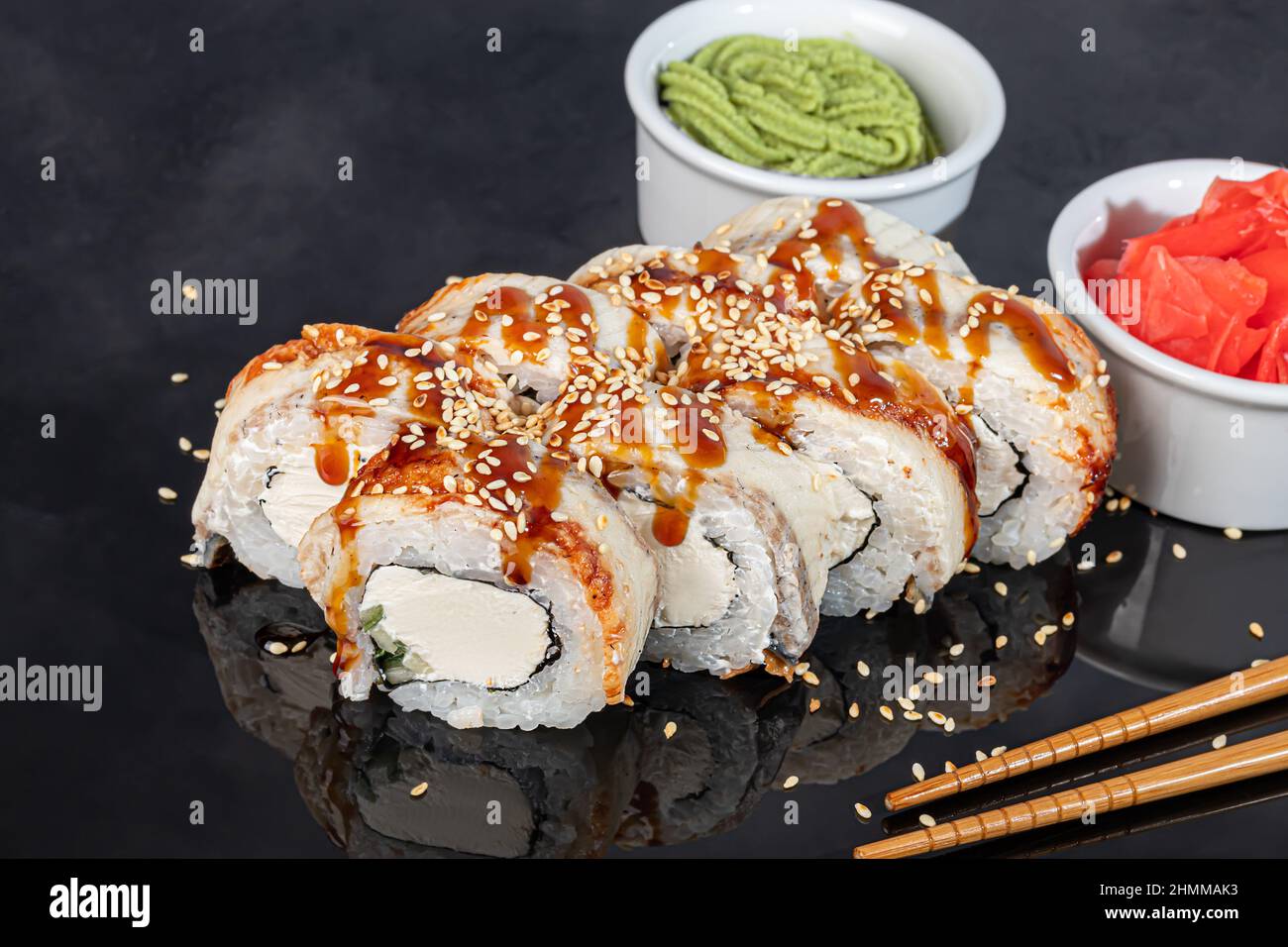 Sushi-Sets Uramaki, California, Philadelphia, Rollen auf einem weißen Teller. Menü für Restaurants, Cafés. Auf einem dunklen reflektierenden Hintergrund Stockfoto