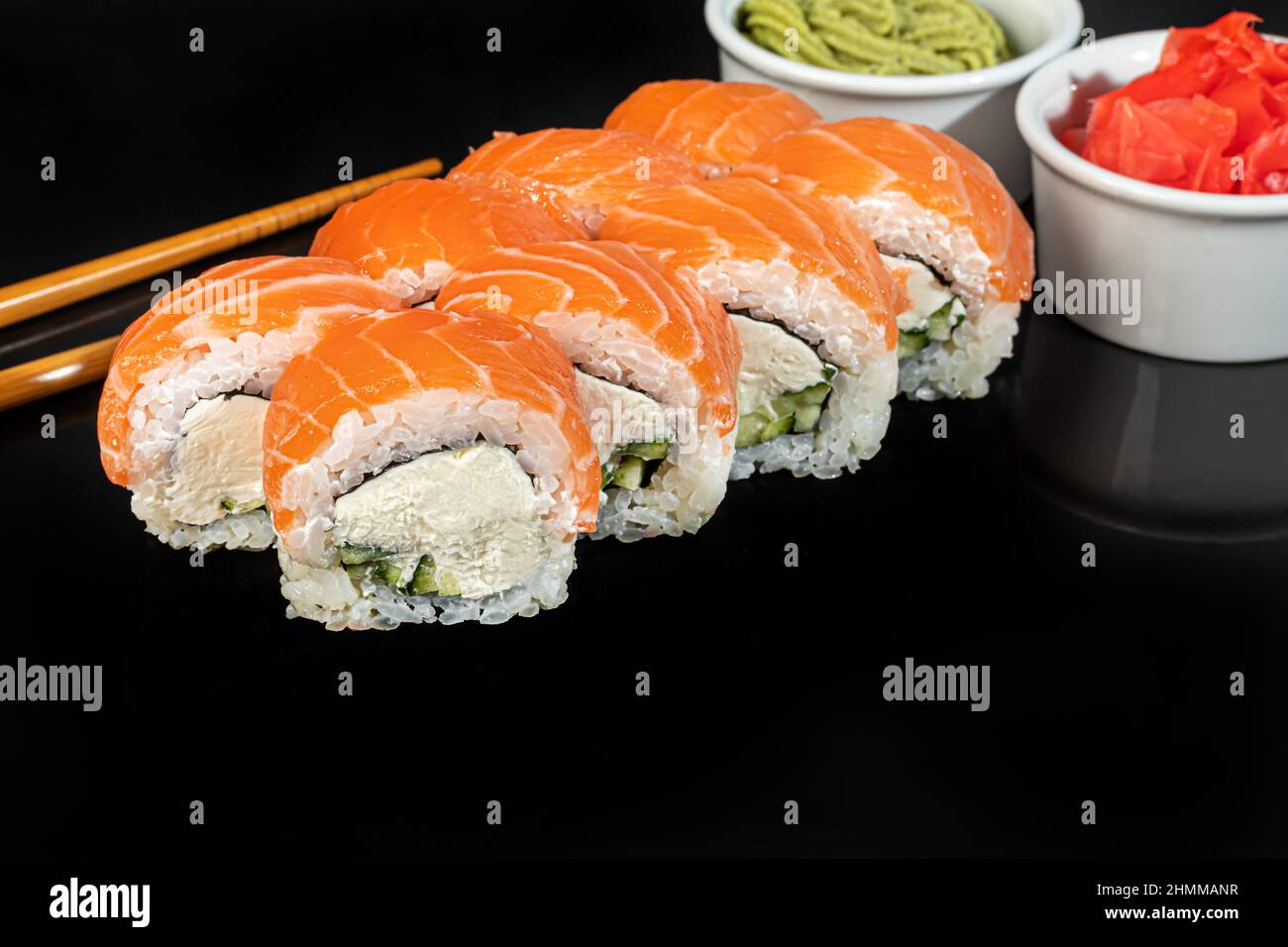 Sushi-Sets Uramaki, California, Philadelphia, Rollen auf einem weißen Teller. Menü für Restaurants, Cafés. Auf einem dunklen reflektierenden Hintergrund Stockfoto