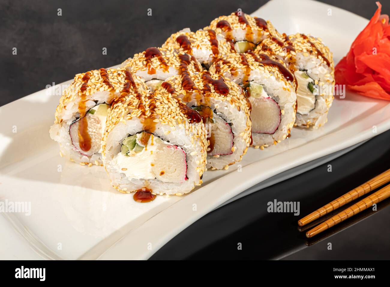 Sushi-Sets Uramaki, California, Philadelphia, Rollen auf einem weißen Teller. Menü für Restaurants, Cafés. Auf einem dunklen reflektierenden Hintergrund Stockfoto