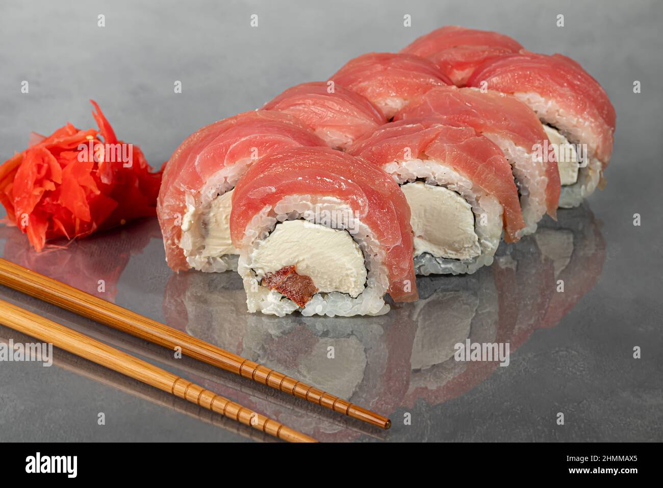 Sushi-Sets Uramaki, California, Philadelphia, Rollen auf einem weißen Teller. Menü für Restaurants, Cafés. Auf einem dunklen reflektierenden Hintergrund Stockfoto