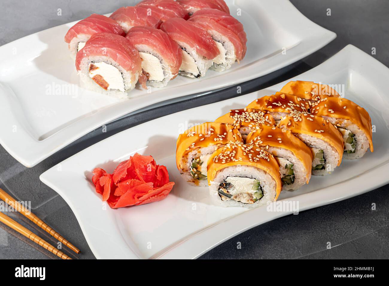 Sushi-Sets Uramaki, California, Philadelphia, Rollen auf einem weißen Teller. Menü für Restaurants, Cafés. Auf einem dunklen reflektierenden Hintergrund Stockfoto
