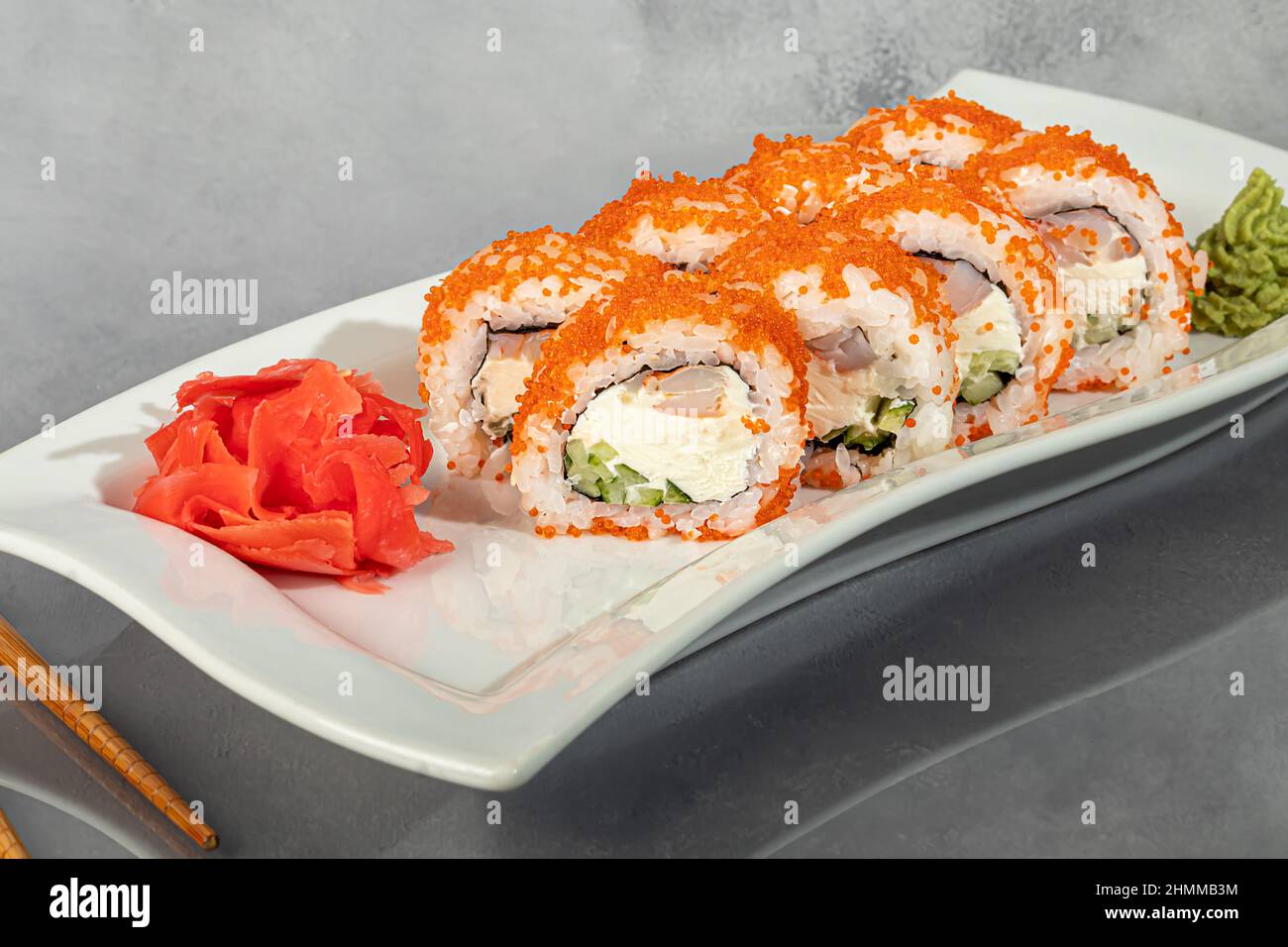 Sushi-Sets Uramaki, California, Philadelphia, Rollen auf einem weißen Teller. Menü für Restaurants, Cafés. Auf einem dunklen reflektierenden Hintergrund Stockfoto