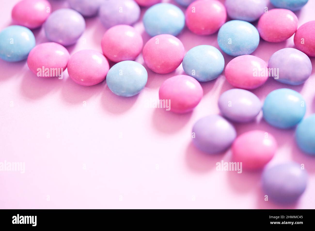 Pastellrosa, blau und lavendellila Smarties Choc Candy auf einem schlichten, hellrosa Hintergrund. Nahaufnahme, feminines Bannerbild für Web und soziale Medien. Stockfoto