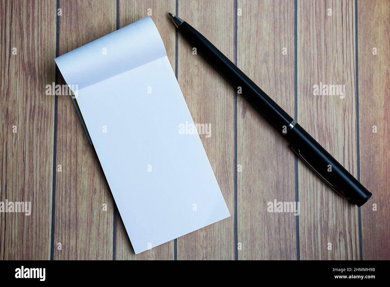 Notizblock mit einem Stift auf einem Holzschreibtisch. Direkt darüber. Flach liegend. Stockfoto