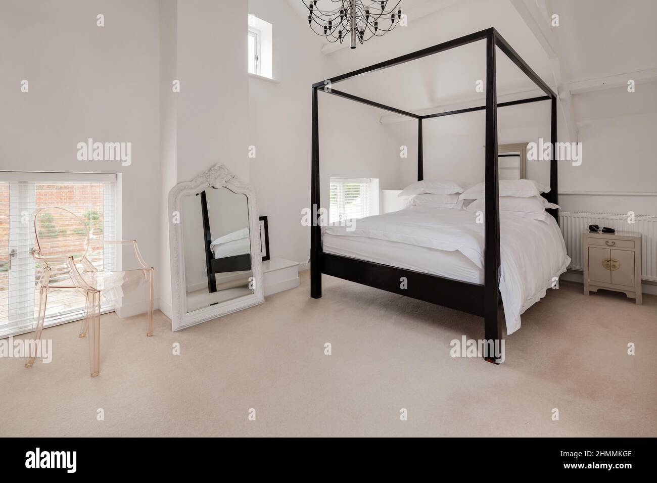 Newport, Essex - Juli 10 2018: Luxuriöses, modern eingerichtetes, schickes Schlafzimmer in Weiß mit Himmelbett aus dunklem Holz und einem auffälligen Spiegel mit kunstvollem Rahmen Stockfoto