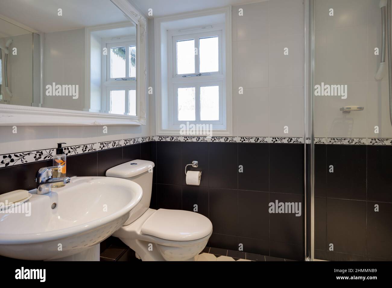 Hemmingford Grey, Cambridgeshire - Feb 10 2018: Kompaktes Duschbad mit komplett gefliesten Wänden und großem Spiegel mit kunstvoll weiß gestrichenen Rahmen. Stockfoto