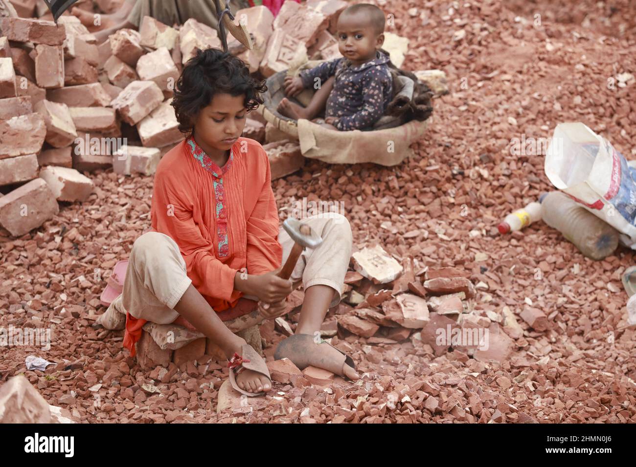 Die Kinder von Bangladesch, Rajiya, 9, brechen Ziegel, die als Kies für den Bau in Dhaka, Bangladesch, verwendet werden sollen, 10. Februar 2022. Kinderarbeit ist in Bangladesch üblich, 4,7 Millionen Kinder im Alter von 5 bis 14 Jahren arbeiten in der Belegschaft. Von den Kinderarbeitern, die in der Belegschaft beschäftigt sind, sind 83 % in ländlichen Gebieten und 17 % in städtischen Gebieten beschäftigt. Im Jahr 2006 verabschiedete Bangladesch ein Arbeitsgesetz, in dem das Mindestalter für eine Beschäftigung auf 14 Jahre festgelegt wurde. Dennoch ist die Durchsetzung solcher Arbeitsgesetze in Bangladesch praktisch unmöglich, da 93 % der Kinderarbeiter im informellen Sektor wie Smal beschäftigt sind Stockfoto