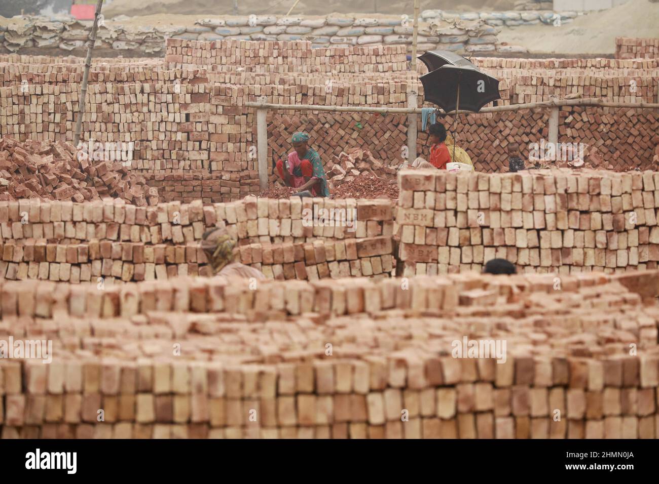 Eine bangladeschische Frau bricht Ziegel, um als Kies für den Bau in Dhaka, Bangladesch, verwendet zu werden, 10. Februar 2022. Kinderarbeit ist in Bangladesch üblich, 4,7 Millionen Kinder im Alter von 5 bis 14 Jahren arbeiten in der Belegschaft. Von den Kinderarbeitern, die in der Belegschaft beschäftigt sind, sind 83 % in ländlichen Gebieten und 17 % in städtischen Gebieten beschäftigt. Im Jahr 2006 verabschiedete Bangladesch ein Arbeitsgesetz, in dem das Mindestalter für eine Beschäftigung auf 14 Jahre festgelegt wurde. Dennoch ist die Durchsetzung solcher Arbeitsgesetze in Bangladesch praktisch unmöglich, da 93 % der Kinderarbeiter im informellen Sektor wie in kleinen Fabriken beschäftigt sind Stockfoto