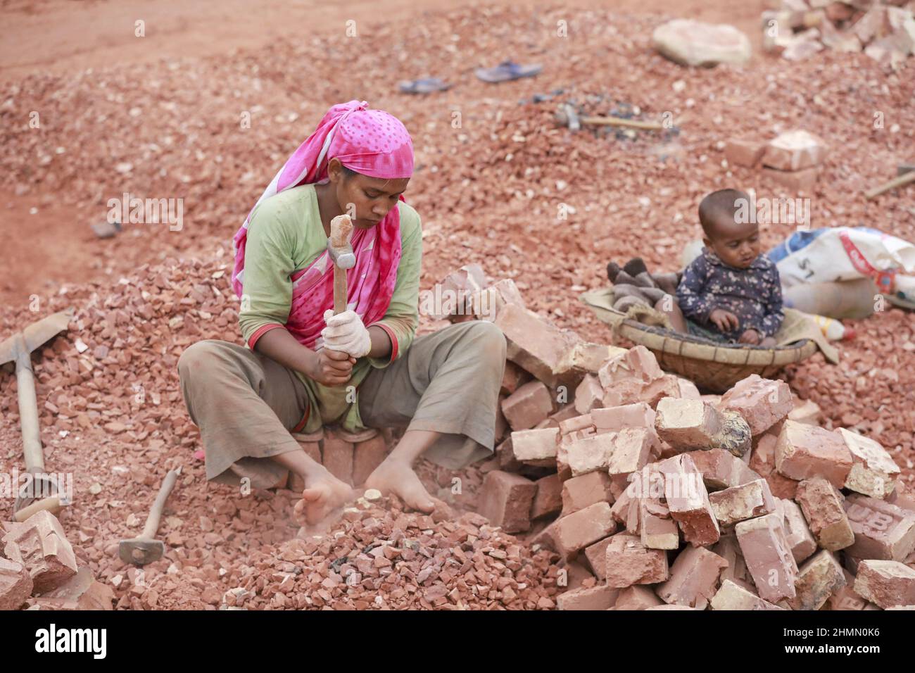 Eine bangladeschische Frau bricht Ziegel, um als Kies für den Bau in Dhaka, Bangladesch, verwendet zu werden, 10. Februar 2022. Kinderarbeit ist in Bangladesch üblich, 4,7 Millionen Kinder im Alter von 5 bis 14 Jahren arbeiten in der Belegschaft. Von den Kinderarbeitern, die in der Belegschaft beschäftigt sind, sind 83 % in ländlichen Gebieten und 17 % in städtischen Gebieten beschäftigt. Im Jahr 2006 verabschiedete Bangladesch ein Arbeitsgesetz, in dem das Mindestalter für eine Beschäftigung auf 14 Jahre festgelegt wurde. Dennoch ist die Durchsetzung solcher Arbeitsgesetze in Bangladesch praktisch unmöglich, da 93 % der Kinderarbeiter im informellen Sektor wie in kleinen Fabriken beschäftigt sind Stockfoto