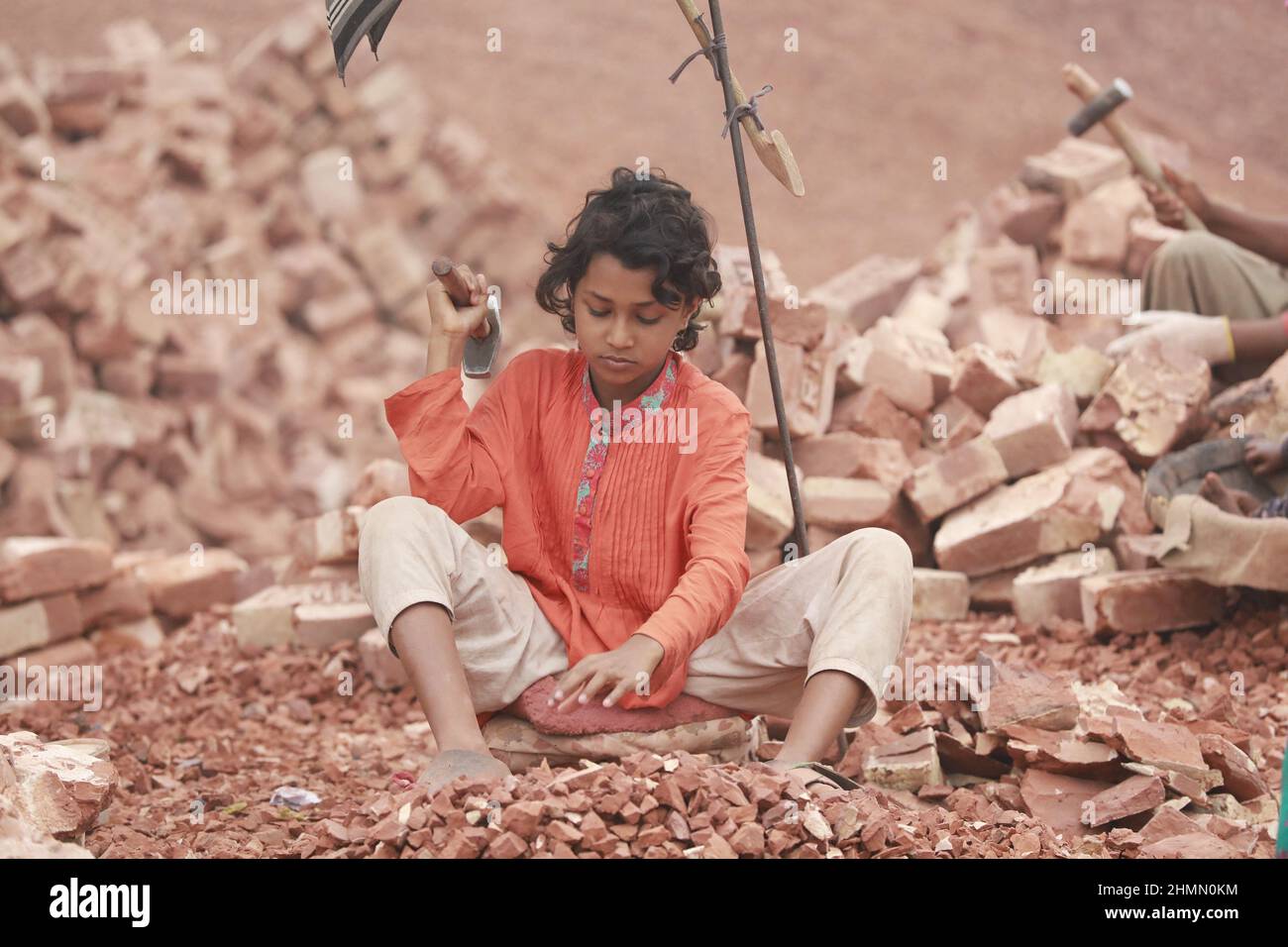 Die Kinder von Bangladesch, Rajiya, 9, brechen Ziegel, die als Kies für den Bau in Dhaka, Bangladesch, verwendet werden sollen, 10. Februar 2022. Kinderarbeit ist in Bangladesch üblich, 4,7 Millionen Kinder im Alter von 5 bis 14 Jahren arbeiten in der Belegschaft. Von den Kinderarbeitern, die in der Belegschaft beschäftigt sind, sind 83 % in ländlichen Gebieten und 17 % in städtischen Gebieten beschäftigt. Im Jahr 2006 verabschiedete Bangladesch ein Arbeitsgesetz, in dem das Mindestalter für eine Beschäftigung auf 14 Jahre festgelegt wurde. Dennoch ist die Durchsetzung solcher Arbeitsgesetze in Bangladesch praktisch unmöglich, da 93 % der Kinderarbeiter im informellen Sektor wie Smal beschäftigt sind Stockfoto