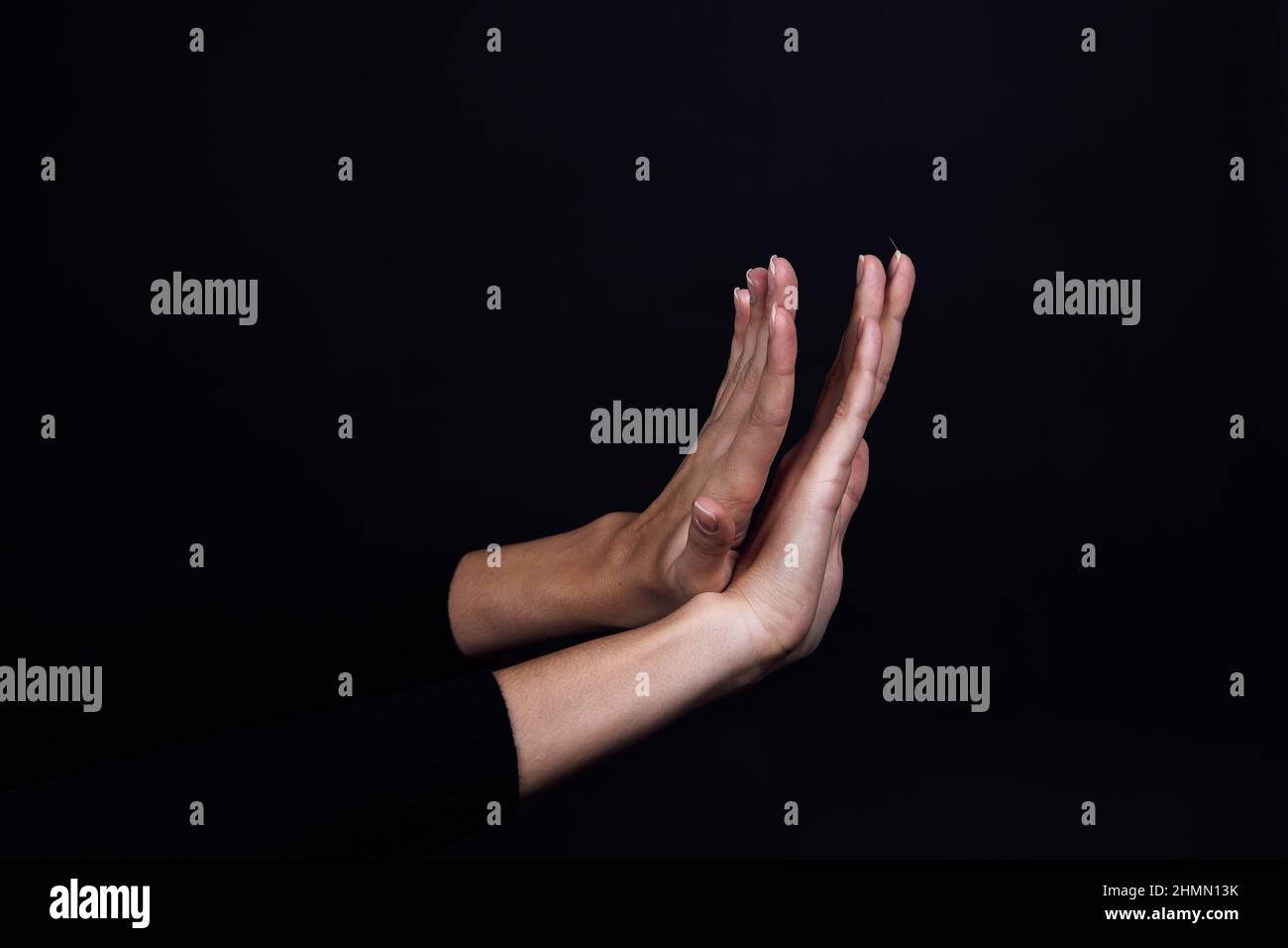 Gekreuzte Hände einer Person auf schwarzem Hintergrund mit Stoppschild. Häuslicher körperlicher, psychologischer Missbrauch, relative Aggression und Gasbeleuchtung. Speicherplatz kopieren Stockfoto