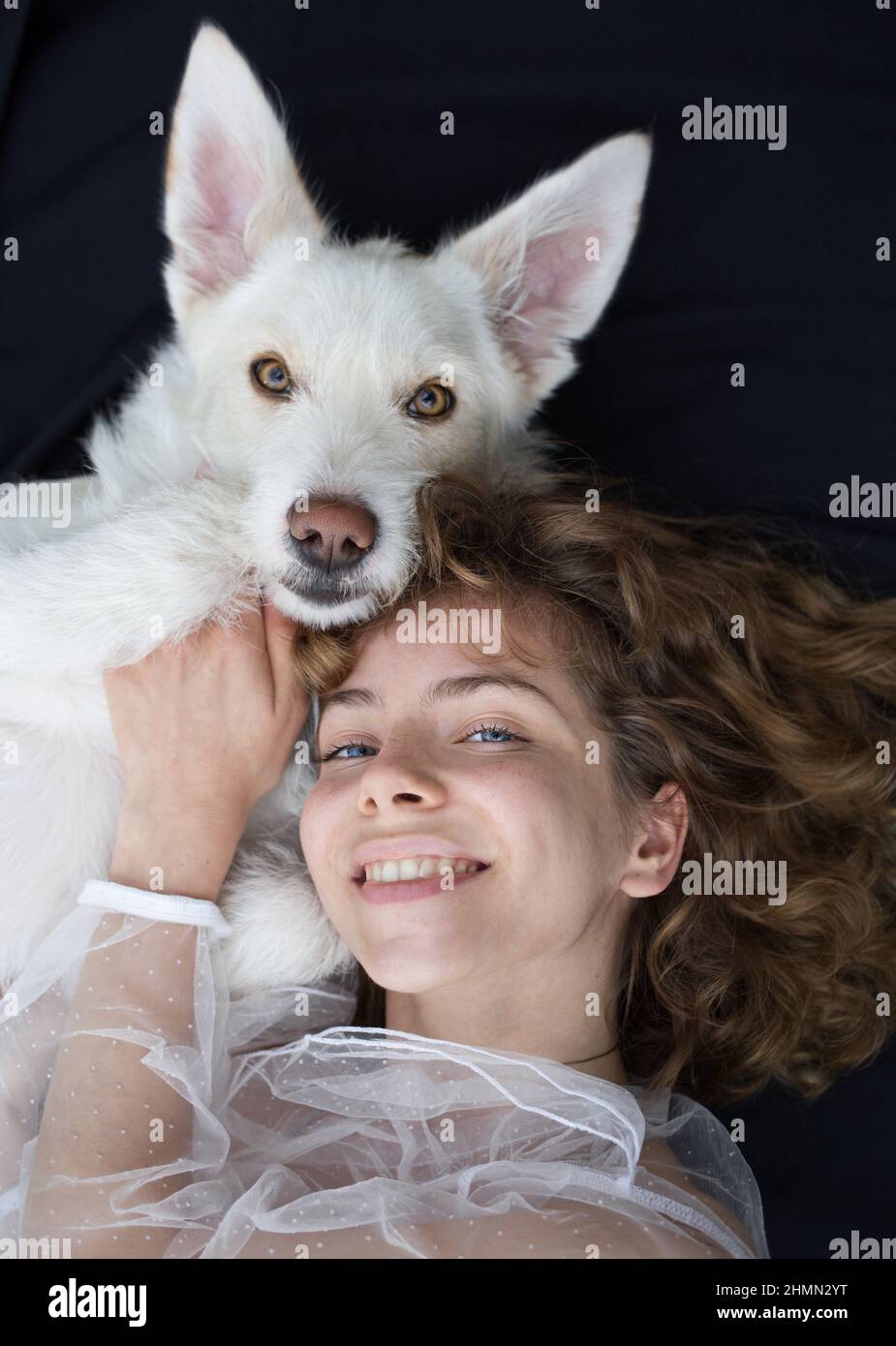 Porträt eines niedlichen Mädchen - ein Teenager von 17-18 Jahren neben ihrem weißen Hund auf einem dunklen Hintergrund. Die Ähnlichkeit und Freundschaft zwischen dem Weibchen o Stockfoto