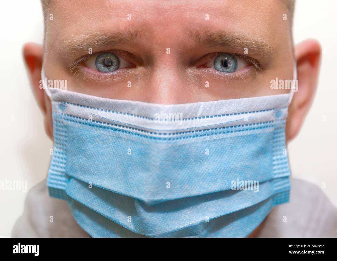 Mann mit intensiven blauen Augen, der eine Gesichtsmaske trägt und direkt auf die Kamera blickt Stockfoto