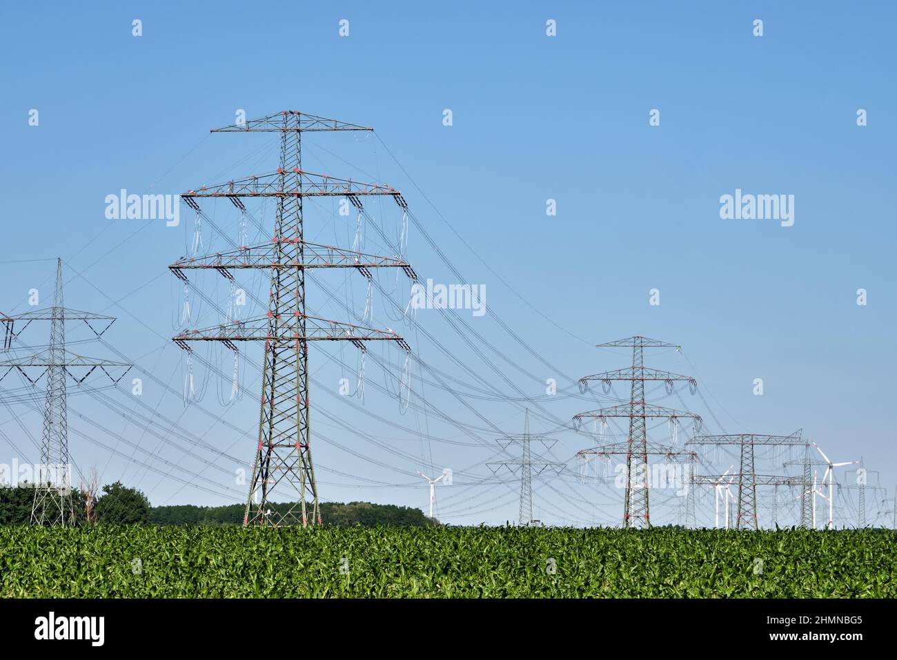 Strommasten und Stromleitungen mit Windturbinen im Hintergrund in Deutschland gesehen Stockfoto