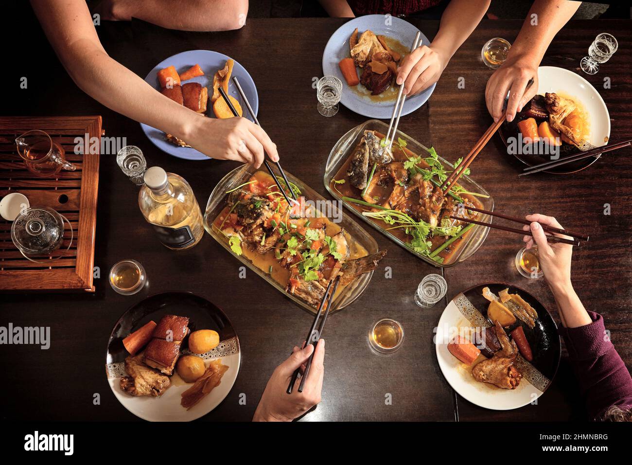 Abendessen mit Freunden am Tisch. Blick von oben. Chinesisches Essen mit Essstäbchen. Fisch, Fleisch, Schweinefleisch, Kartoffeln. Stockfoto