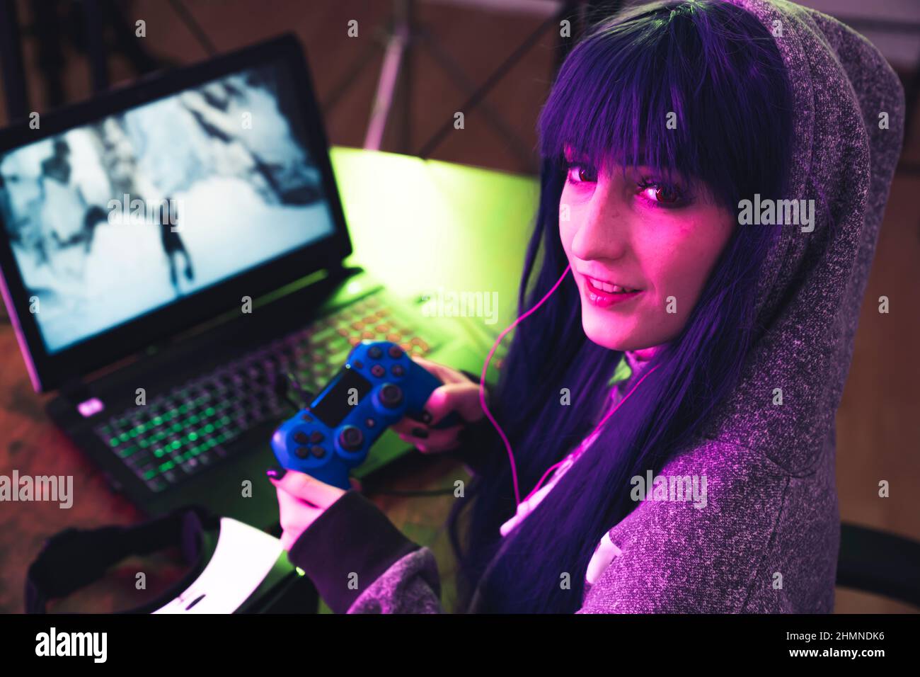 Die junge Brünette in einem Hoodie verwendet Gamepad und ermutigt sie, mit ihrer mittleren Nahaufnahme zu spielen. Hochwertige Fotos Stockfoto