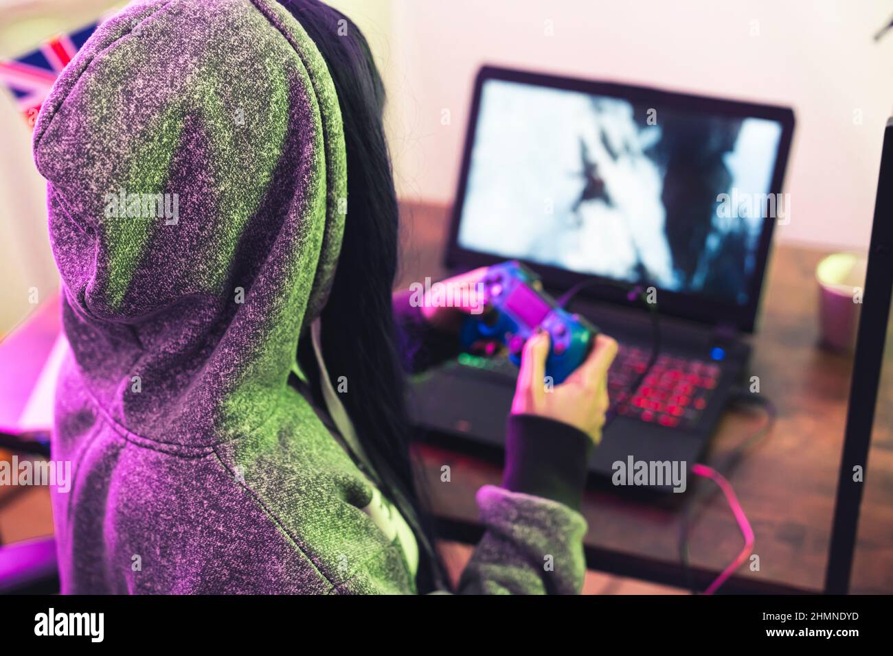Die junge Brünette in einem Hoodie verwendet Gamepad und ermutigt sie, mit ihrer mittleren Nahaufnahme zu spielen. Hochwertige Fotos Stockfoto