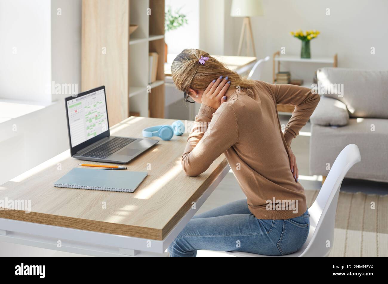 Eine Frau, die in sitzender Haltung auf ihrem Laptop arbeitet, leidet unter Rückenschmerzen Stockfoto