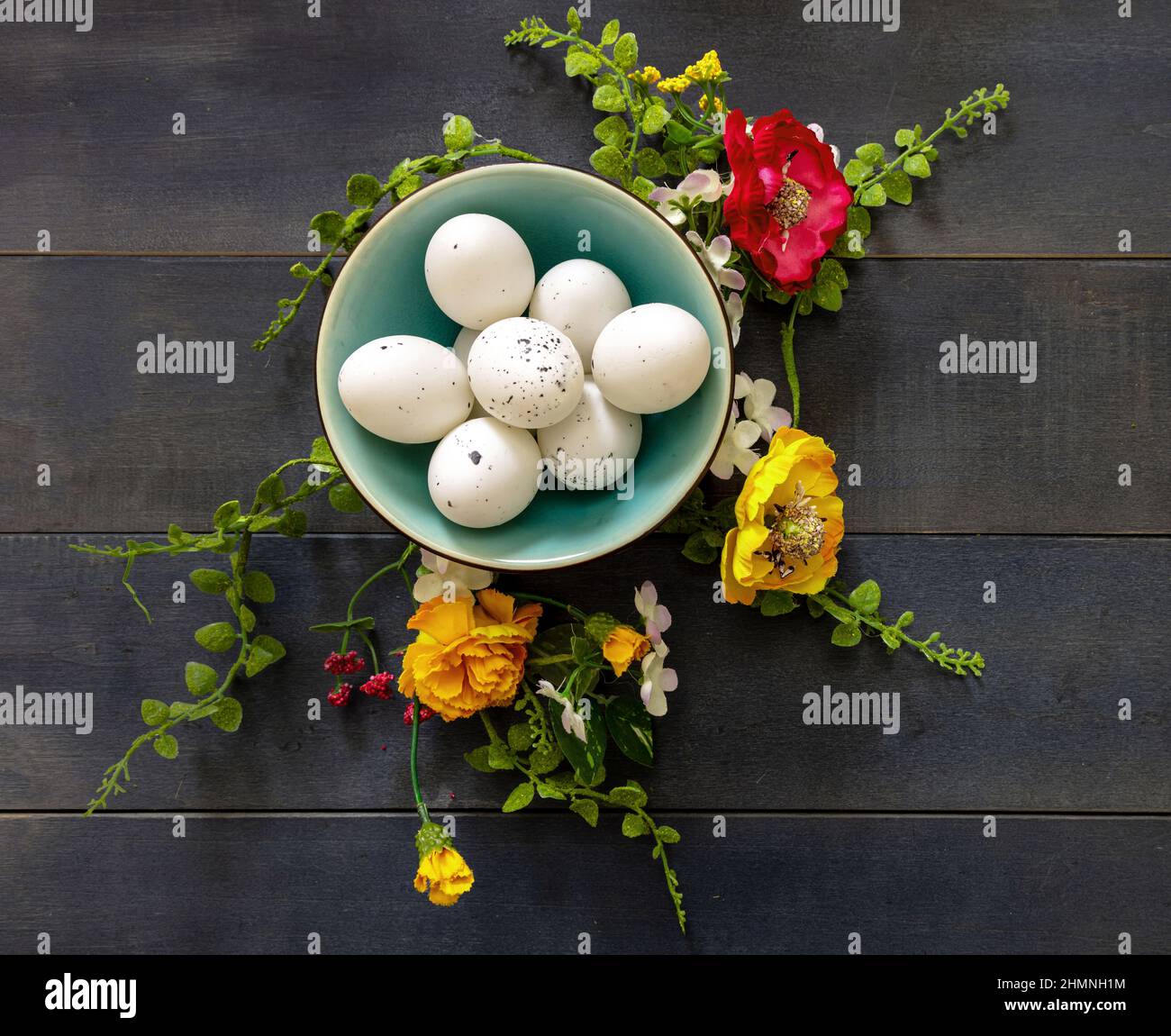 Osterurlaub Im Frühling. Wachtelei in einer Keramikschale und Blumendekoration, blauer Holztischhintergrund, Draufsicht. Natürliche gesunde Lebensmittel Stockfoto