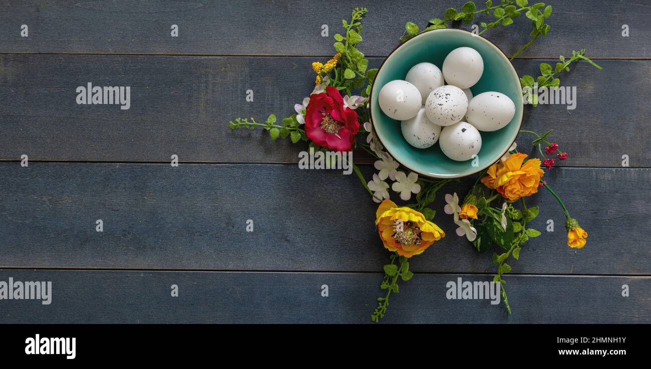 Frohe Ostern. Wachtelei in einer Keramikschale und Frühlingsblumendekoration, blauer Holztischhintergrund, Draufsicht, Kopierraum. Grußkartenvorlage Stockfoto