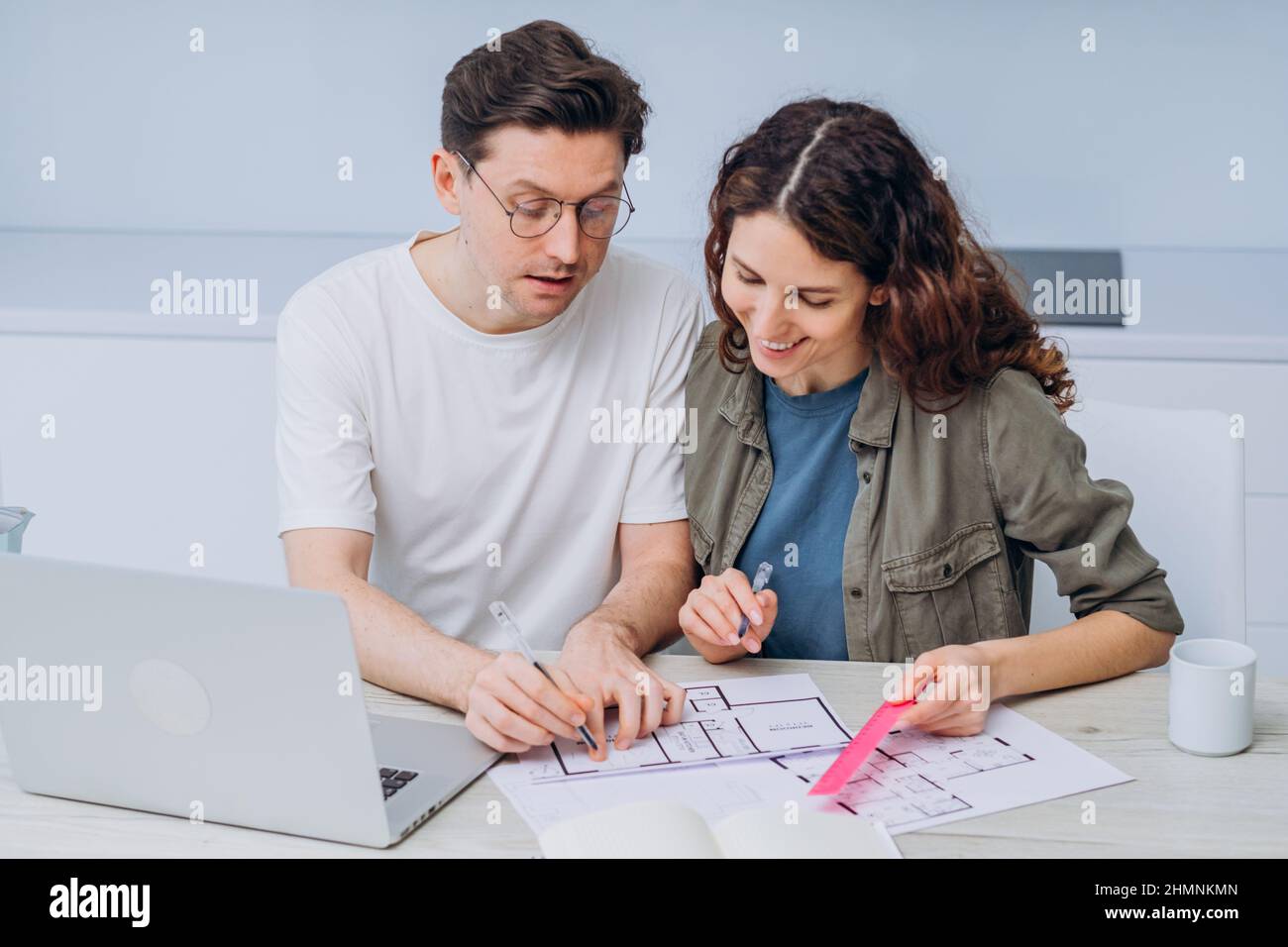 Das Paar sitzt in der Küche, trinkt Kaffee zum Frühstück und spricht über Zeichnungen von Wohnungsrenovierungen, die Notizen in Laptop und Notebook machen Stockfoto