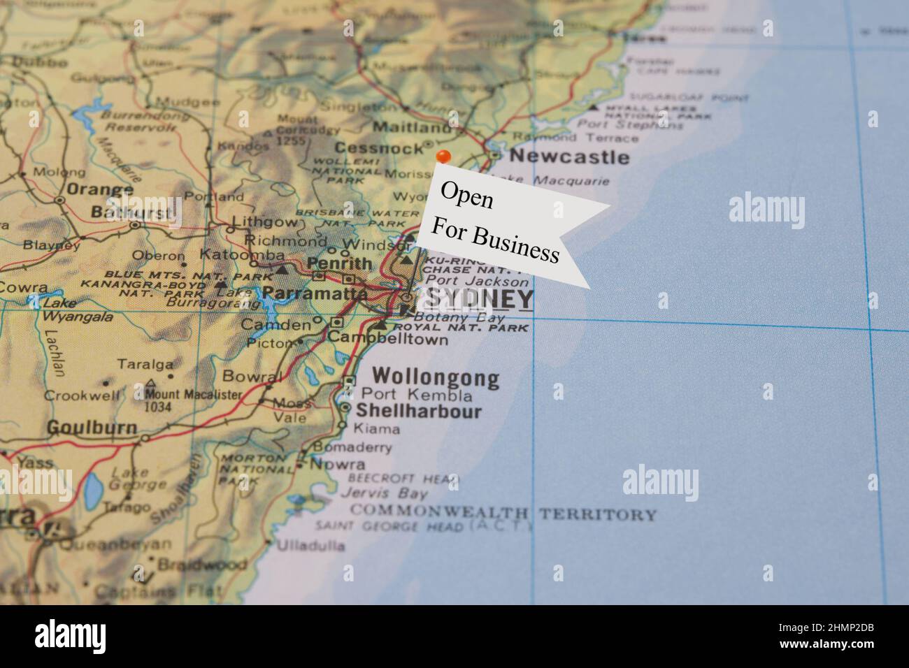 Eine Nahaufnahme einer kleinen Flagge mit dem Satz „Open for Business“ an einer Nadel, die in Sydney, Australien, in einem Atlas platziert wurde Stockfoto