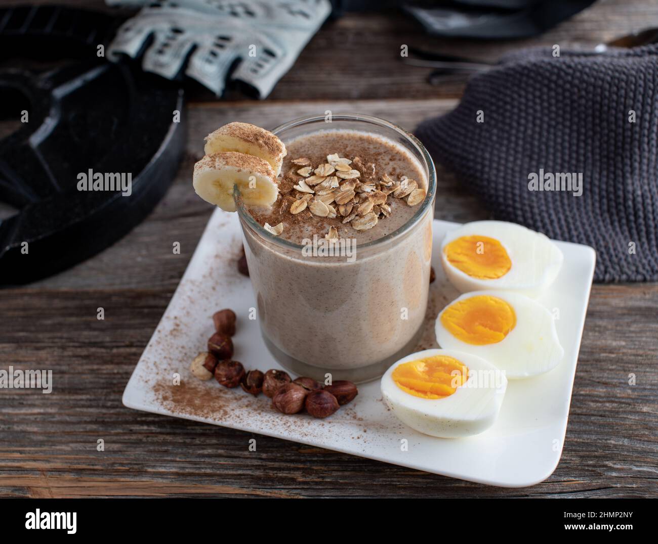 Bodybuilding-Frühstück für Muskelaufbau mit einem Schokoladenprotein-Smoothie aus Molke, Bananen, Haselnüssen und Haferflocken. Serviert mit gekochten Eiern Stockfoto