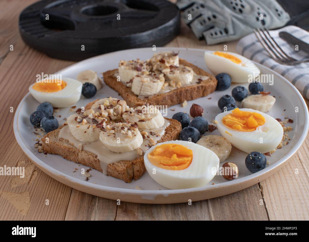 Frühstücksteller mit hohem Kaloriengehalt für Muskelaufbau und Massengewinn mit gekochten Eiern, Toast, Mandelbutter, Bananen und Haselnüssen Stockfoto