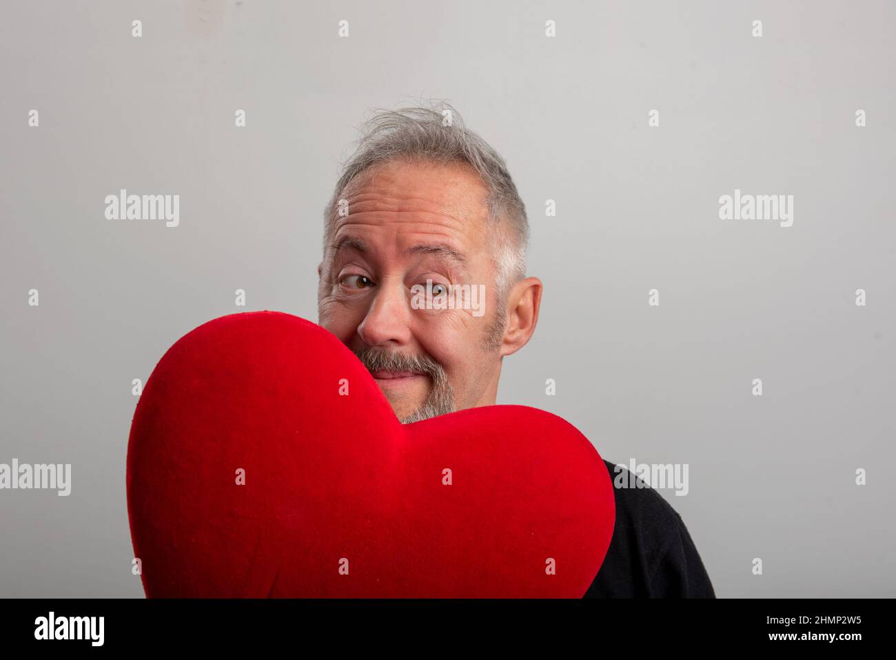 Schöner grauhaariger und bärtiger Mann mittleren Alters mit einem roten Herzen und isoliertem grauen Hintergrund. Valentinstag-Konzept Stockfoto
