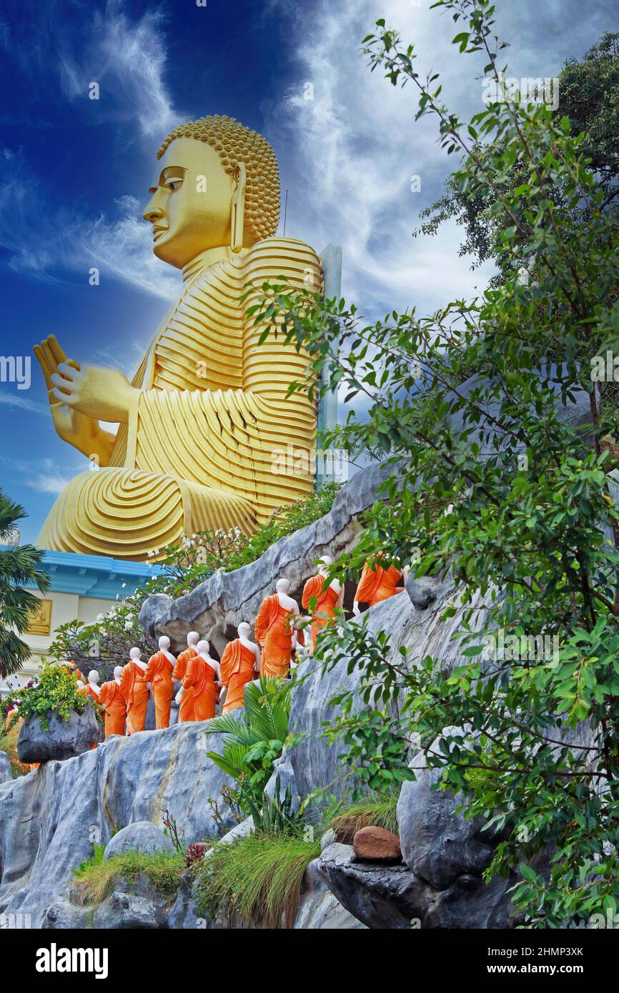 Niedriger Winkel Blick auf goldene buddha-Statue gegen blauen Himmel mit Reihe von buddhistischen Mönchsskulpturen - Dambulla Tempel, Sri Lanka Stockfoto