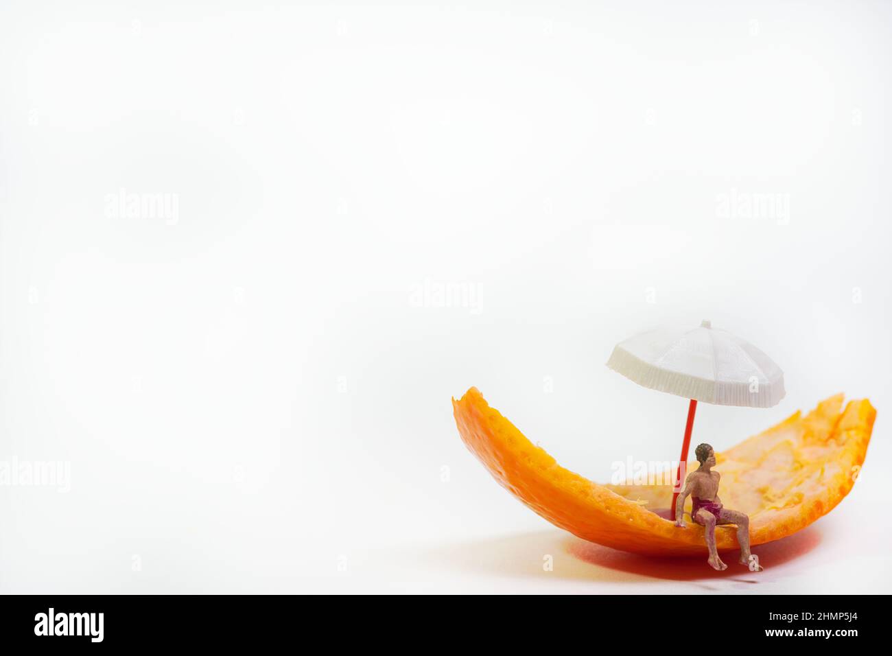 Ein Mann in Badehosen sitzt auf einer Mandarinenschale unter einem Regenschirm Stockfoto