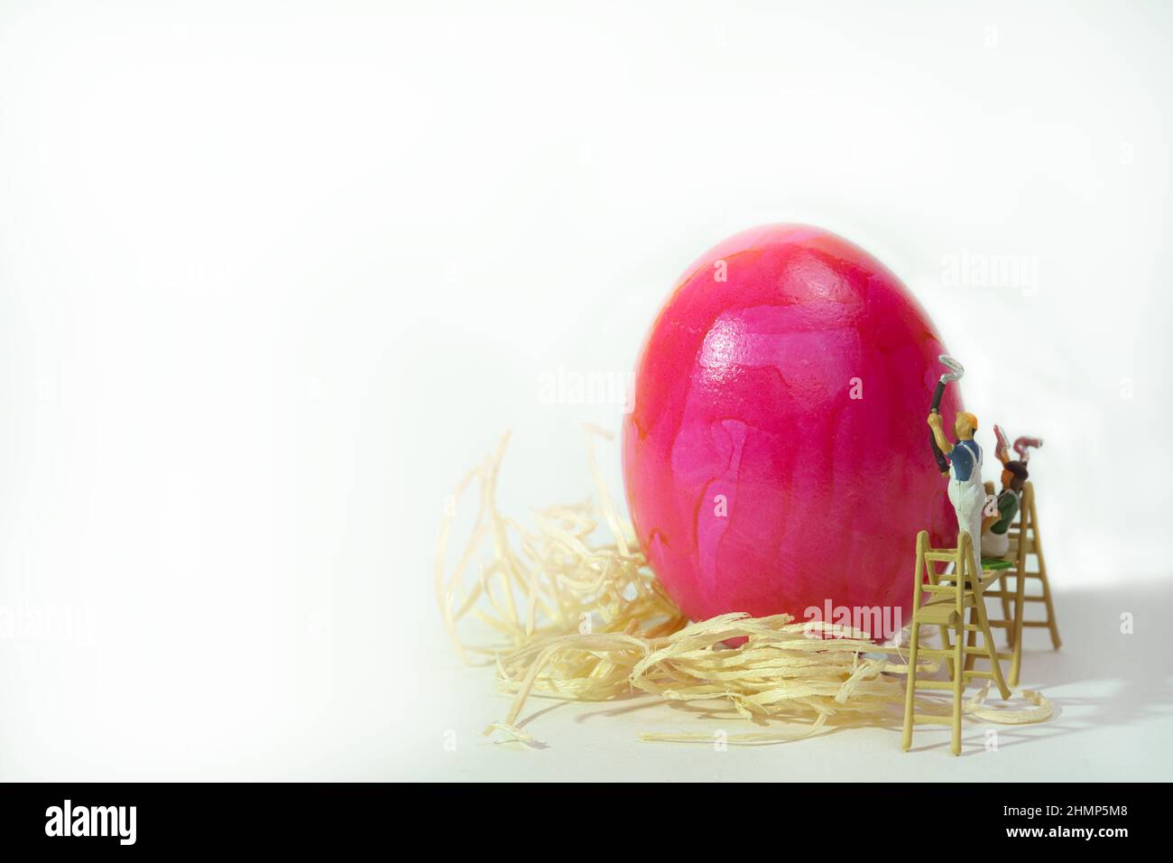 Ein gekochtes rosafarbenes Ei auf Stroh wird von einem Malerteam bemalt Stockfoto