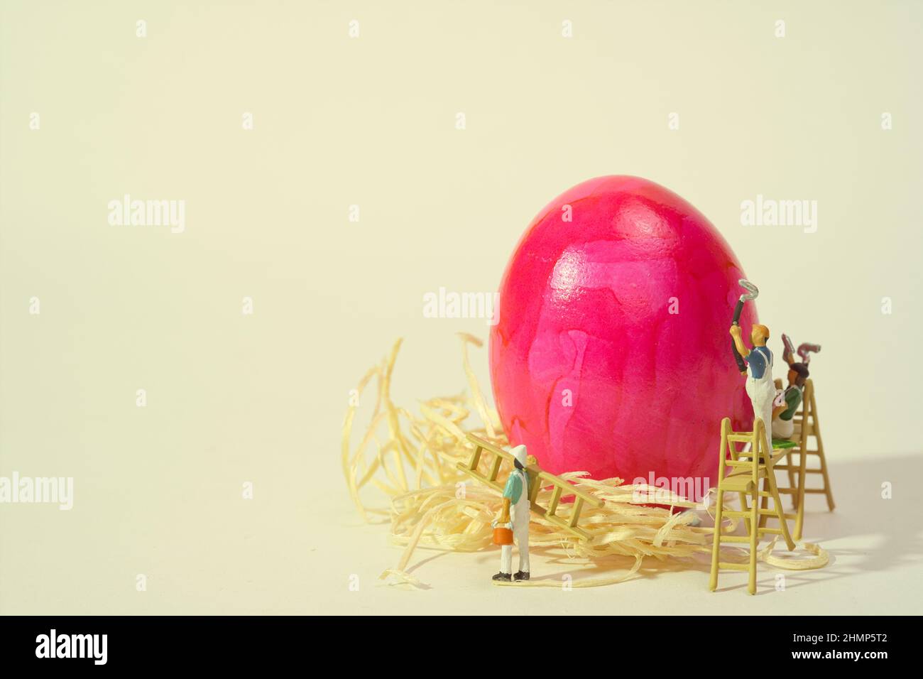 Ein gekochtes rosafarbenes Ei auf Stroh wird von einem Malerteam gemalt Stockfoto
