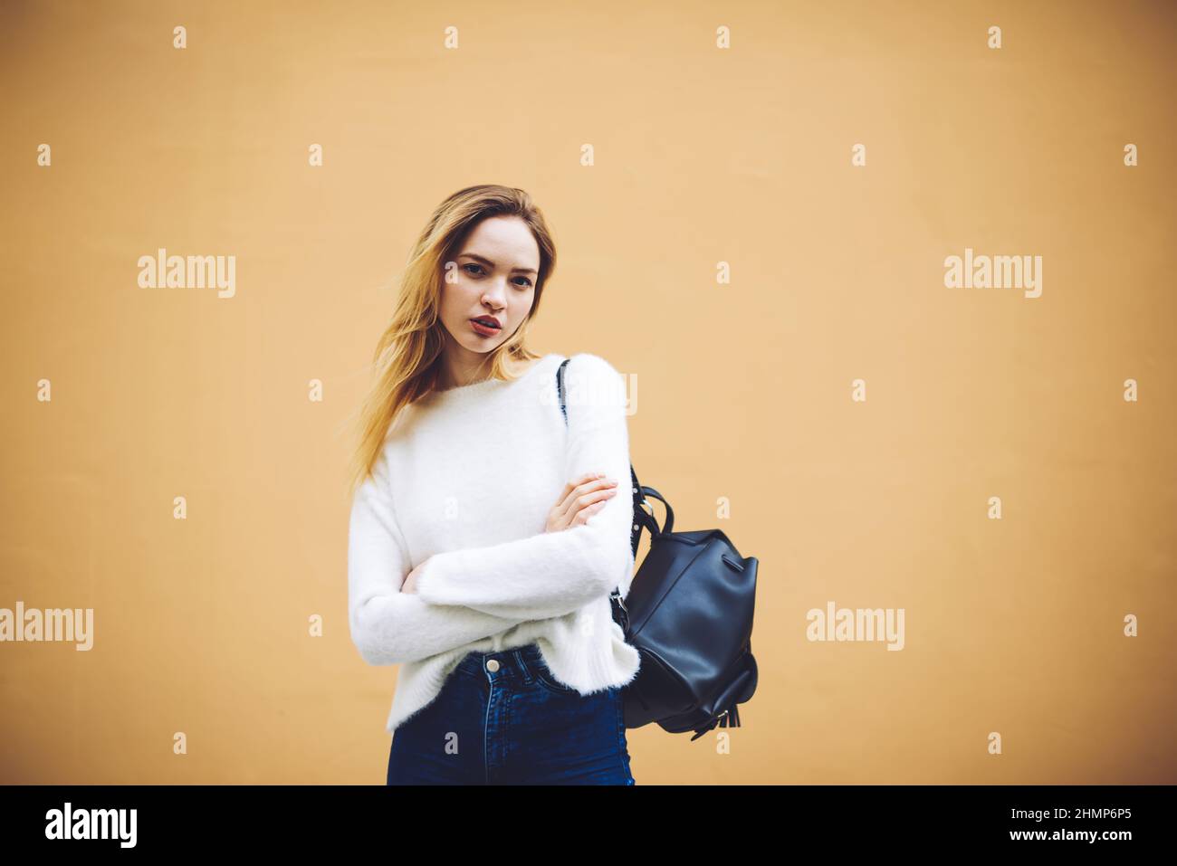 Frau, die an einer braunen Wand mit gekreuzten Armen steht Stockfoto