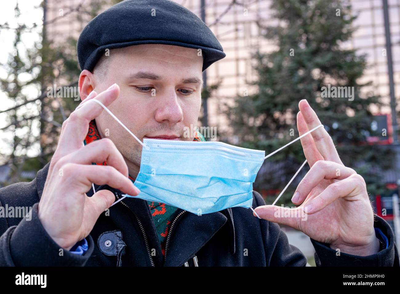 Ein junger Mann, der seine schützende Gesichtsmaske aufsetzt. Im Freien. Maßnahmen zum Schutz des Coronavirus. Stockfoto