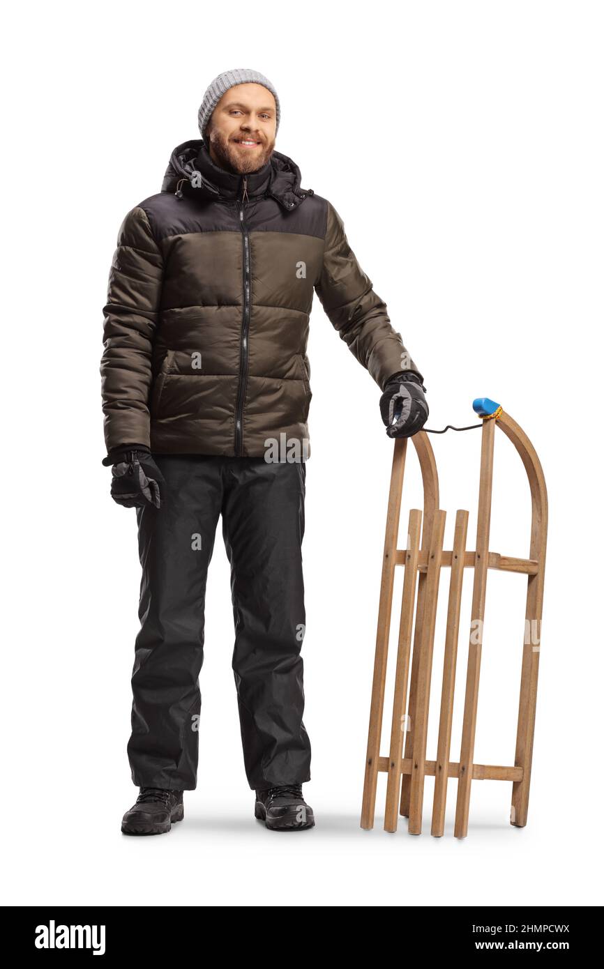 In voller Länge Porträt eines lächelnden jungen Mannes in Winterkleidung stehend mit einem Schlitten isoliert auf weißem Hintergrund Stockfoto