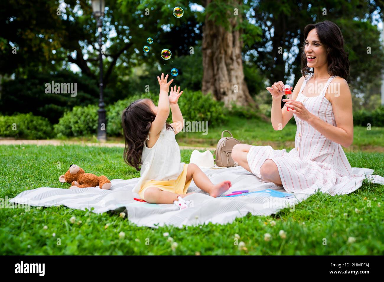 Fröhliche Mama und Tochter spielen mit Blasen im Park Stockfoto